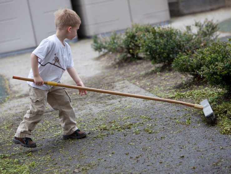 Young boy helping with chores by brushing leaves off of the driveway
