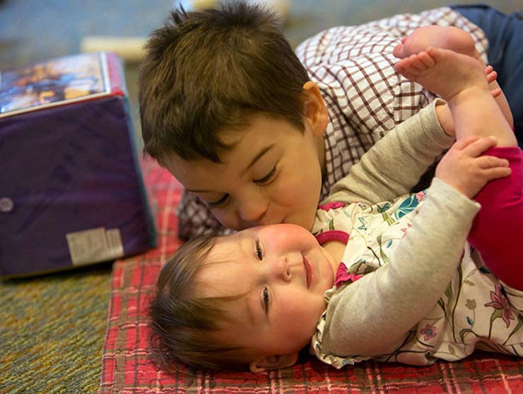 Preschool brother kissing his baby sister on the cheek