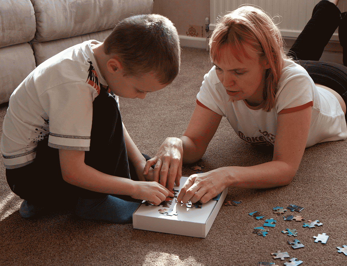 A mom helping her son make a puzzle on the floor.