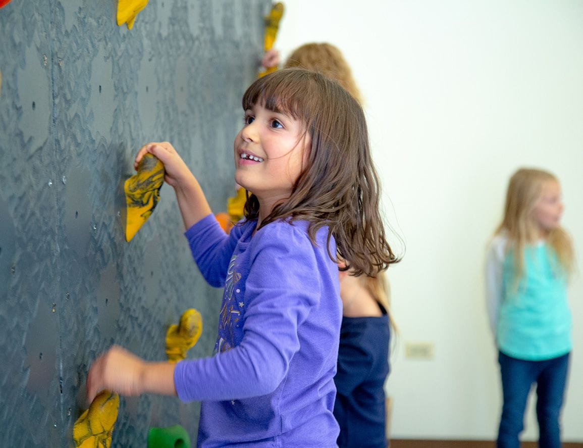 young girls confidently climbing a rock wall