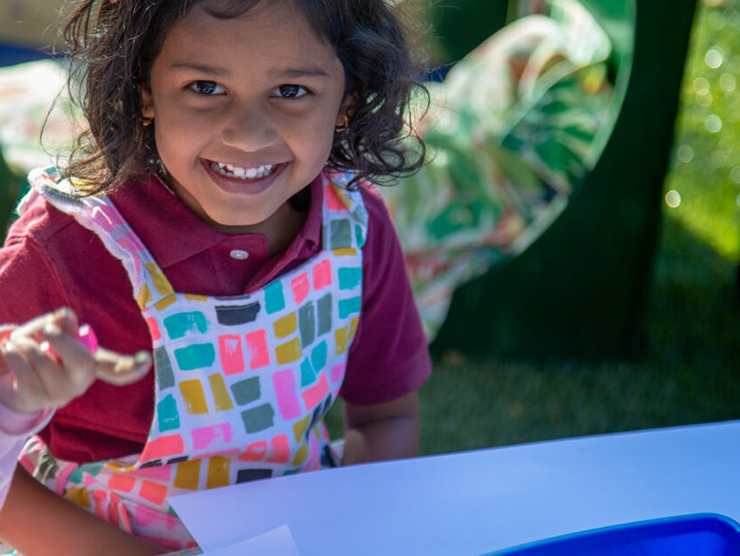 Toddler with a huge smile on her face outside at day care doing arts and crafts 