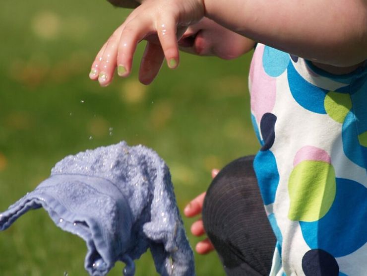 Toddler outside at day care playing with a bucket of water and a wet towel