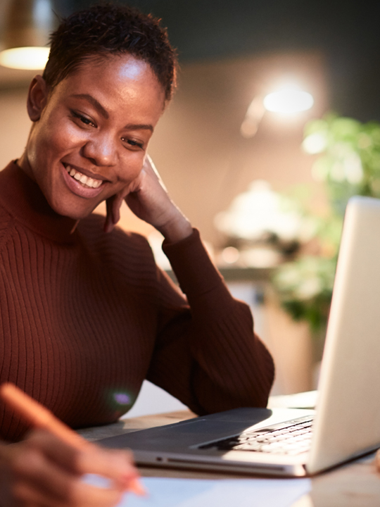 woman at her desk working on laptop and taking notes smiling