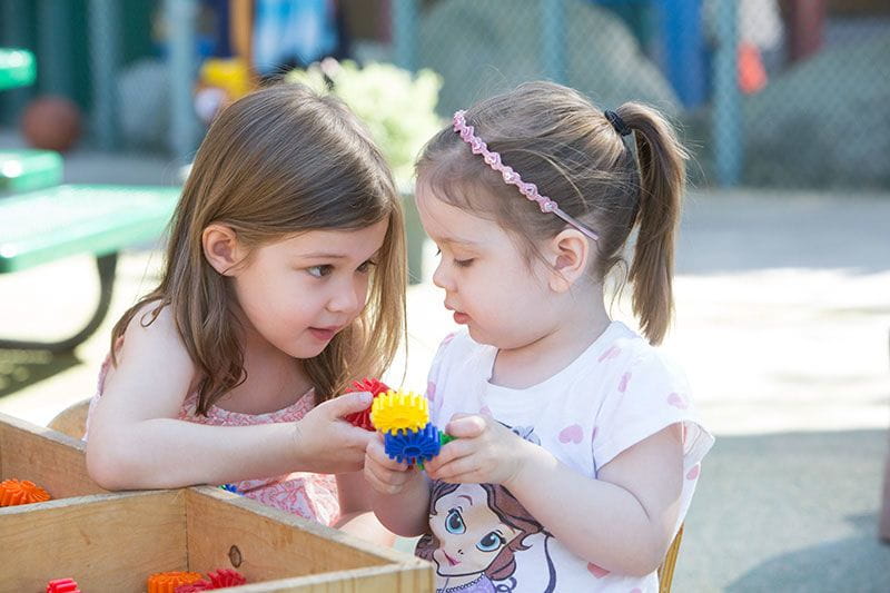 A 3 year old preschool student playing with a 4 year old pre-kindergarten student