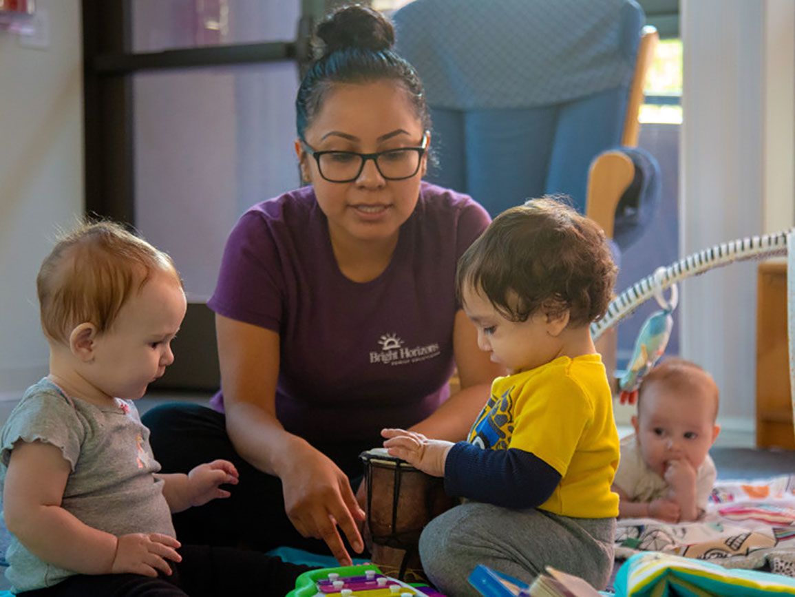 Two toddlers and a teacher interacting with each other in a daycare center