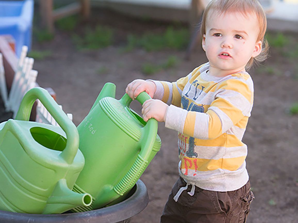 Toddler with water cans for gardening in the city