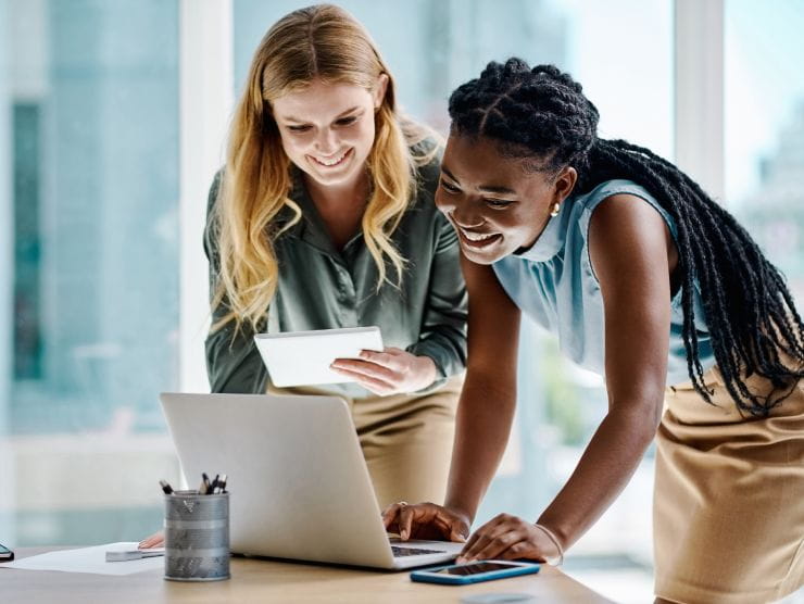 Two female coworkers smiling as they look at a laptop