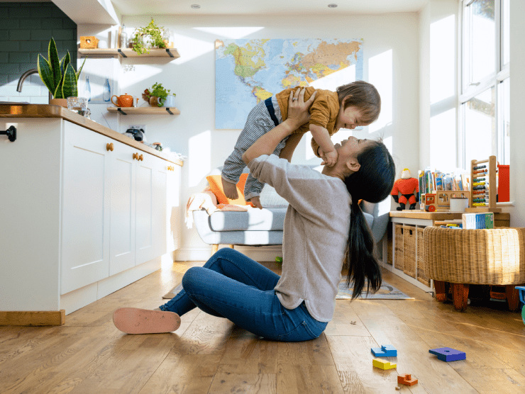 A mother who is sitting on the floor and lifting her child in the air