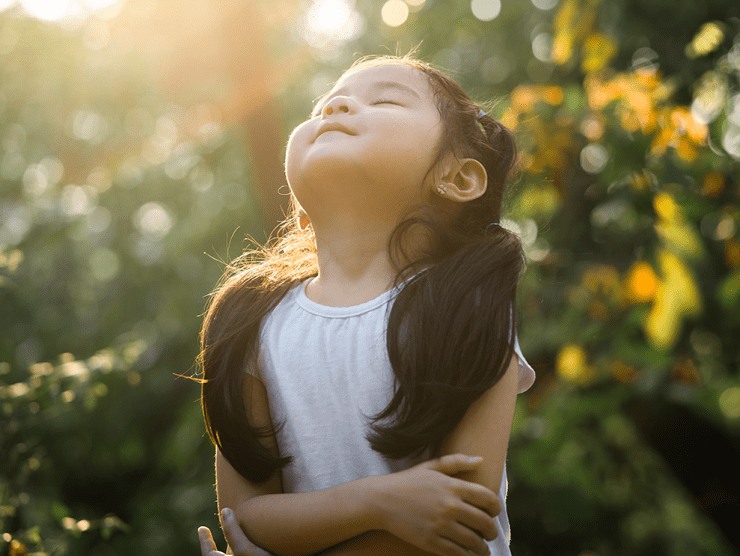 Girl closing her eyes and smiling as the sun shines down on her face