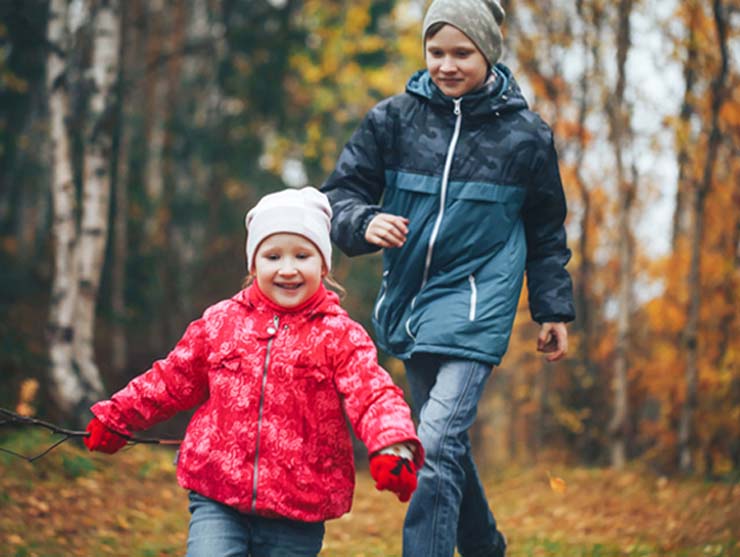 older brother and younger sister playing in the woods