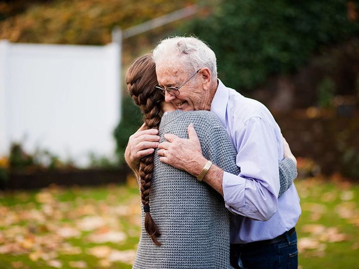 A daughter and elderly father hugging each other.