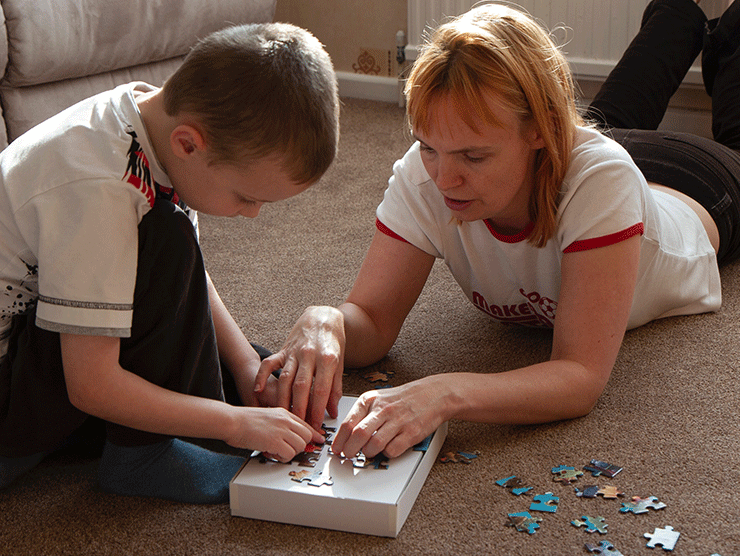 A mom helping her son make a puzzle on the floor.